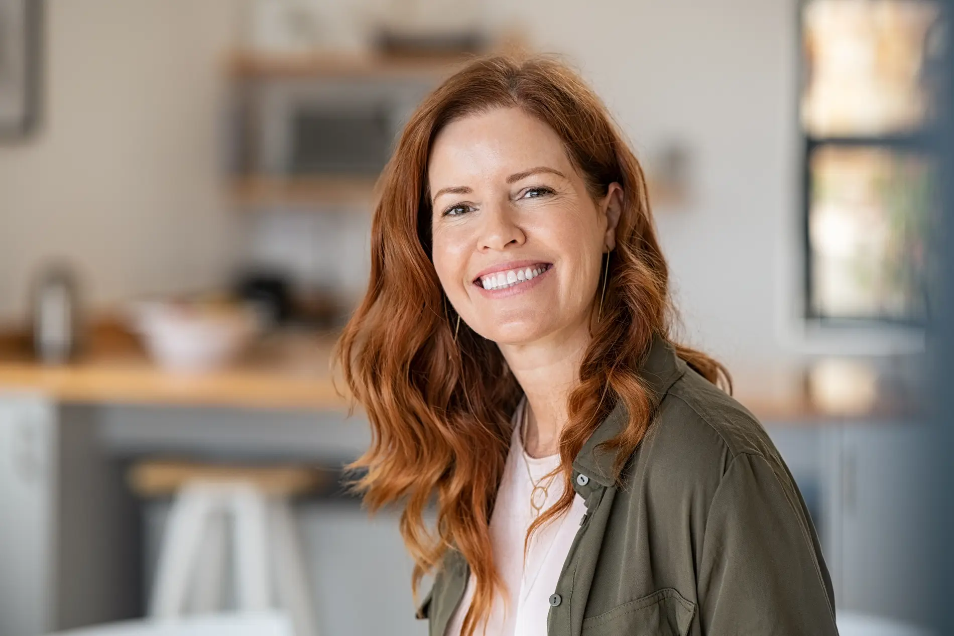 Co2 Fractional Laser And Radiofrequency 1 Smiling Woman With Red Hair In A Cozy Kitchen Setting.